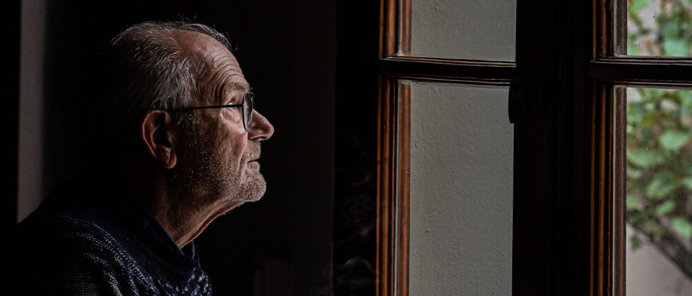 Person sitting alone by a window, highlighting isolation risks.